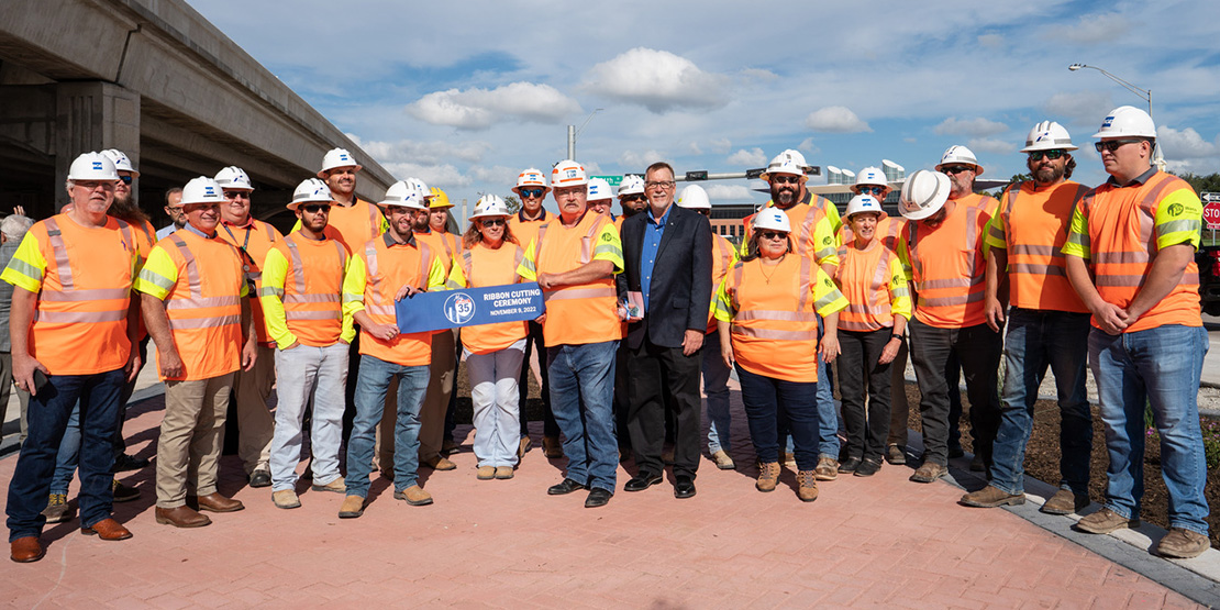 Construction workers holding a ribbon about to be cut in celebration of the completion of the IH 35 Waco 4B reconstruction