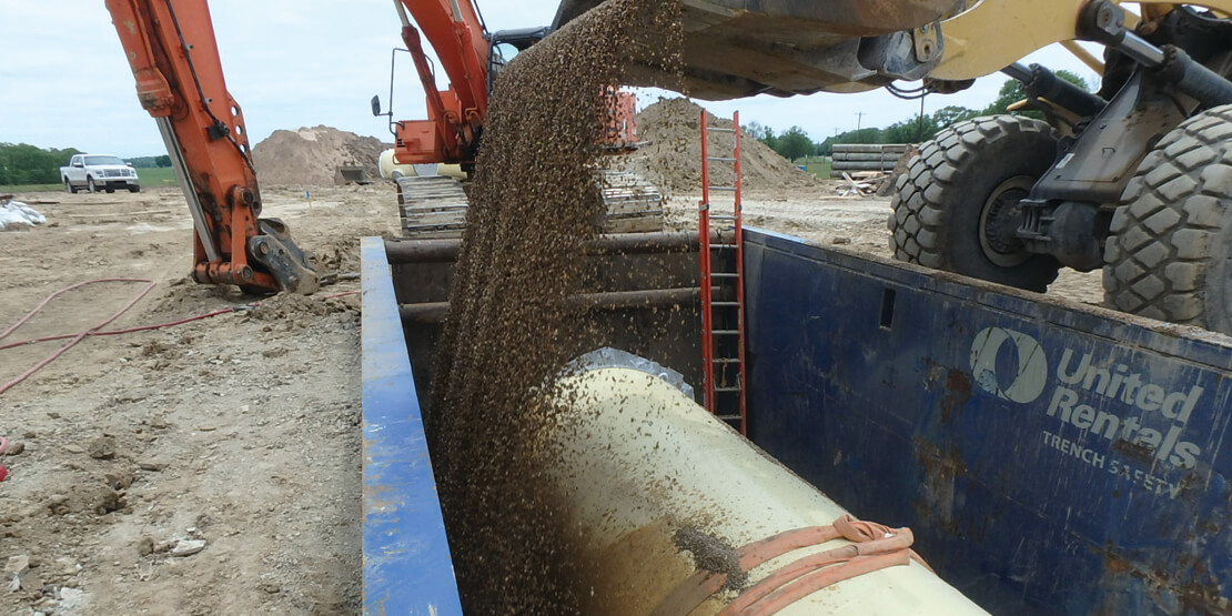 A bulldozer pouring dirt over a water pipe