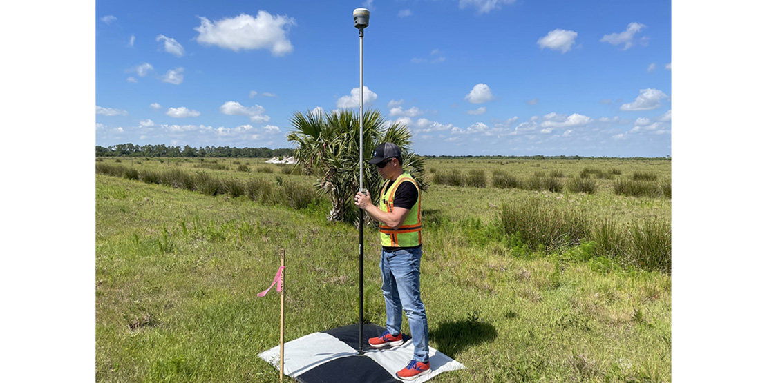 A BGE team member in a yellow hazard vest setting up survey equipment in a field