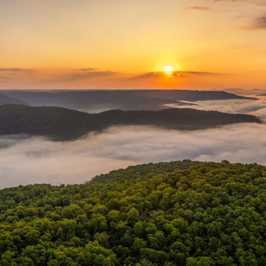 A scenic view of green, tree covered Arkansas hills with fog in the valleys