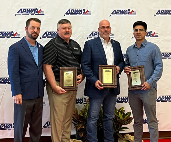 BGE team members holding awards and standing against an APWA banner