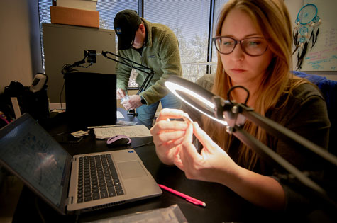 A BGE team member looking over a tiny piece of equipment with a ring light