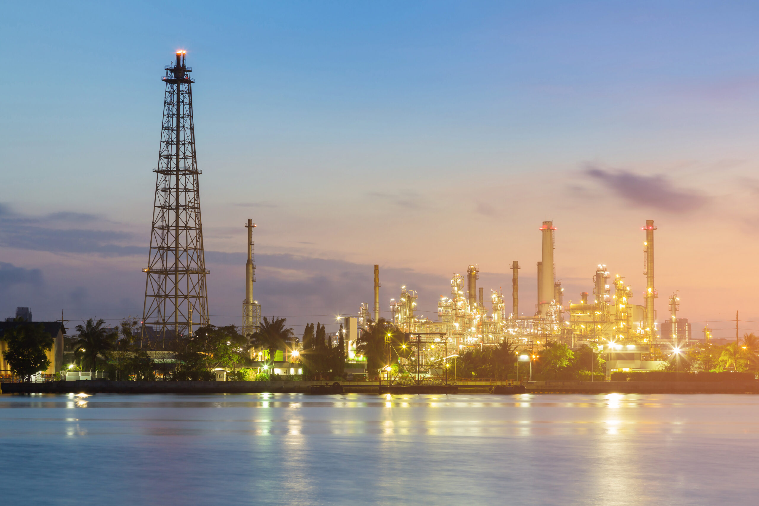 Chemical plant at sunset with water in the foreground, showcasing industrial equipment and structures.